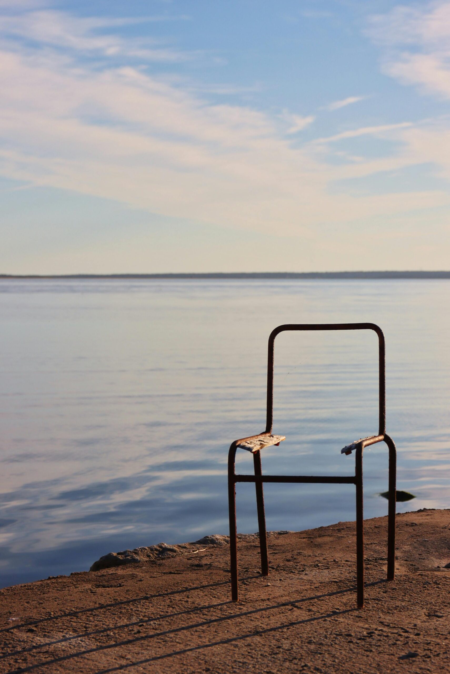 pexels-photo-34892268-34892268 A weathered chair on a serene lakeshore under a vibrant sunset sky.