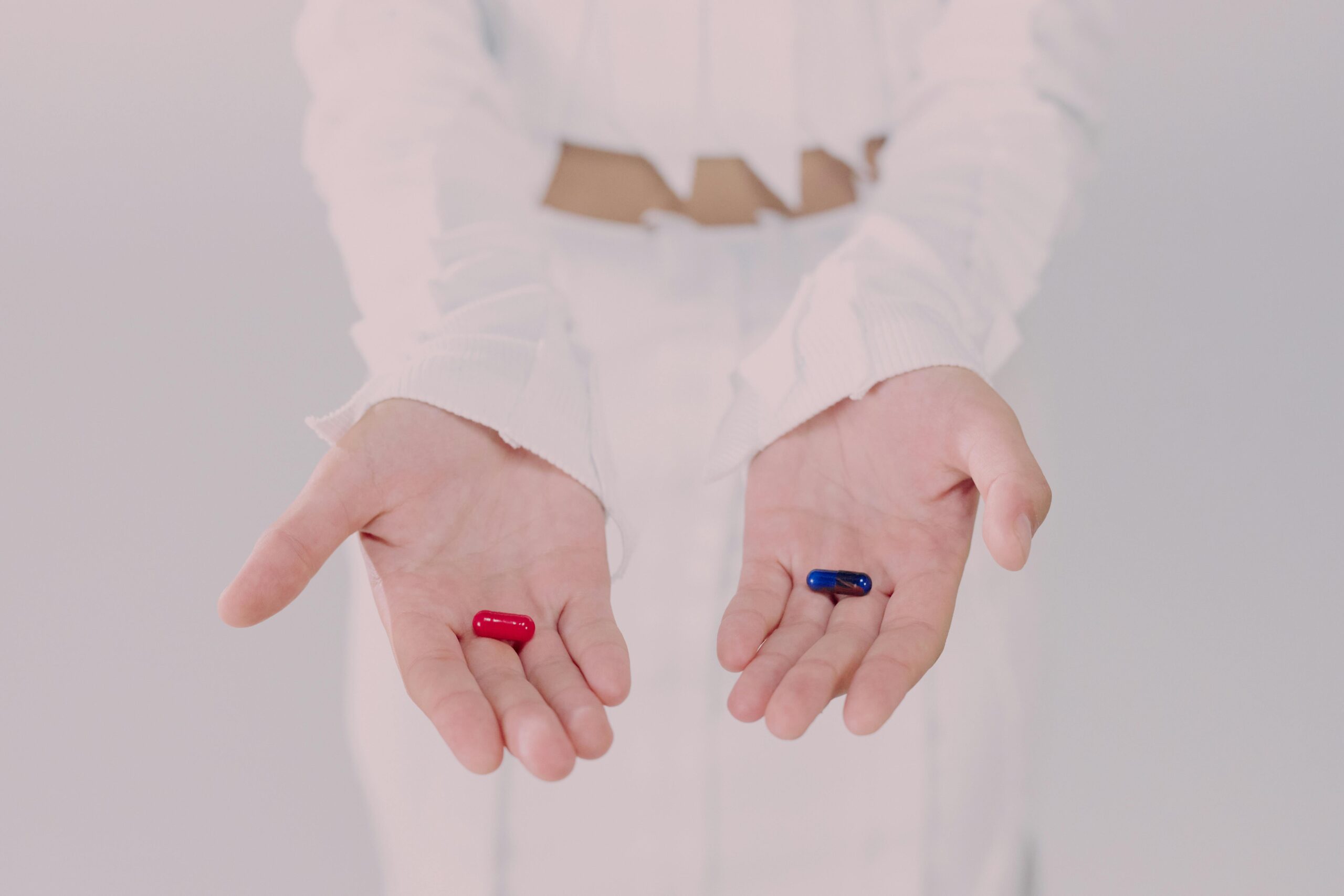 Close-up of hands holding red and blue pills, symbolizing a choice. Conceptual studio shot.